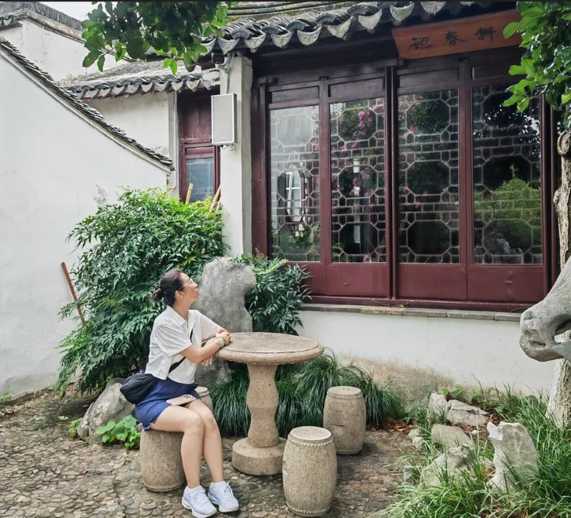 Founder - Eastern Botanical Aesthetics The founder of The Plant World sitting in a classic Chinese botanical garden, surrounded by historic architecture, green trees, and traditional stone elements.
