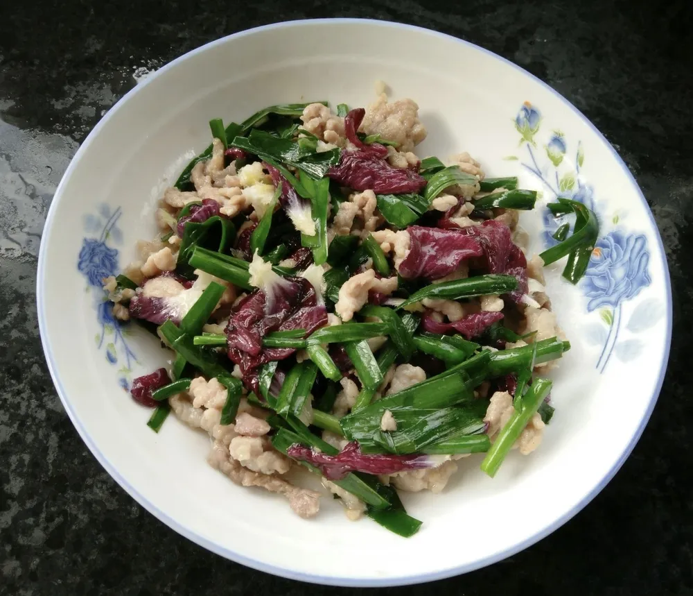 A plate of colorful Chinese stir-fry featuring bright purple hollyhock petals, green garlic chives, and tender shredded pork.