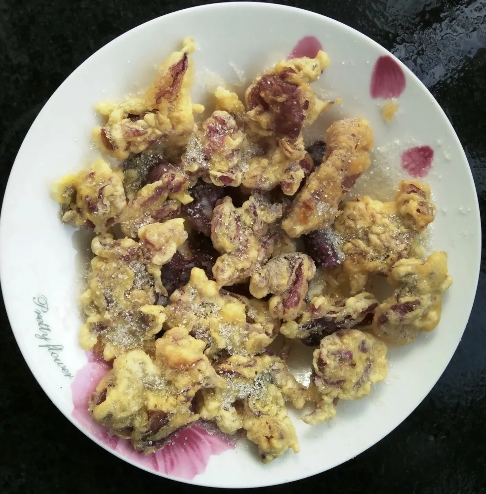 A plate of crispy, egg-battered deep-fried red hollyhock flower petals dusted with granulated white sugar.