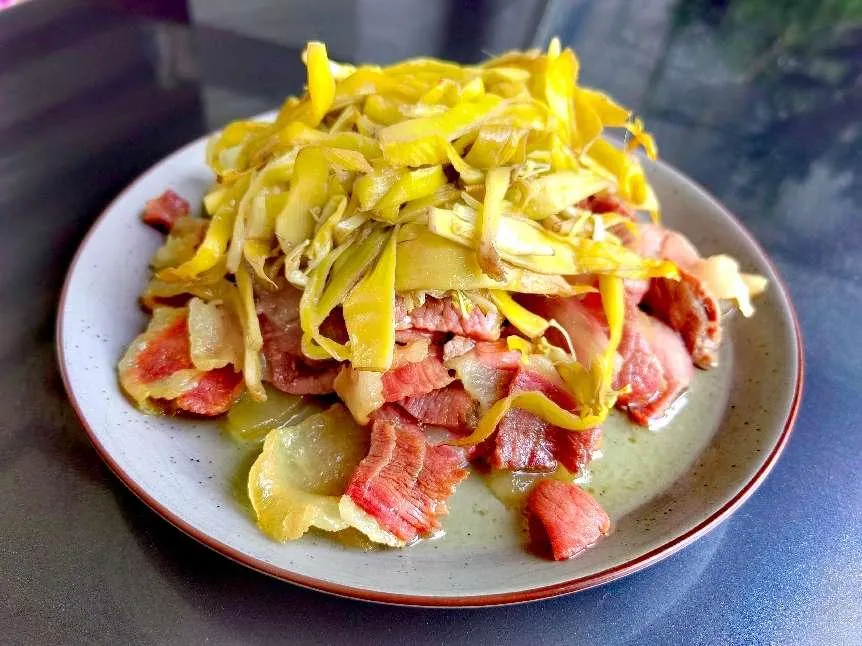 Traditional Southwest Chinese ethnic dish: stir‑fried Golden Lotus Banana flower buds with cured pork meat on ceramic plate