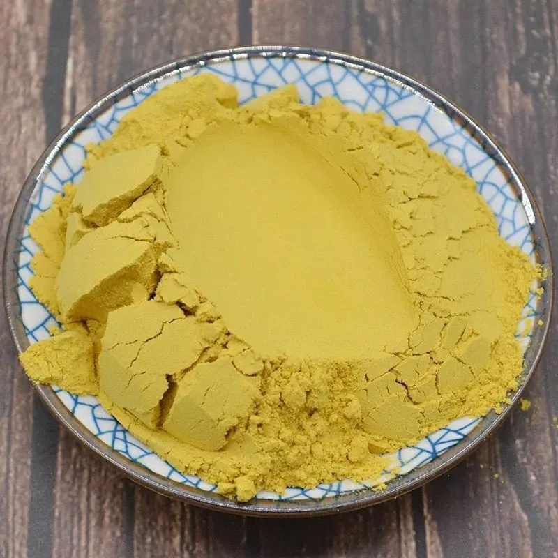 Fine golden-yellow cattail pollen powder (Pollen Typhae / Puhuang) placed on a small ceramic dish over a wooden table.